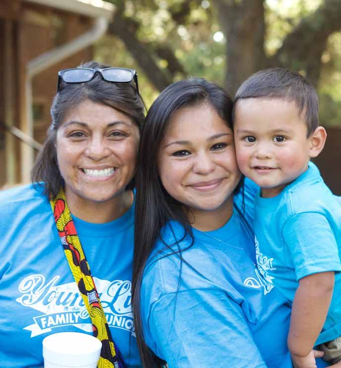 A young mom, her little boy, and a mentor smiling together outdoors