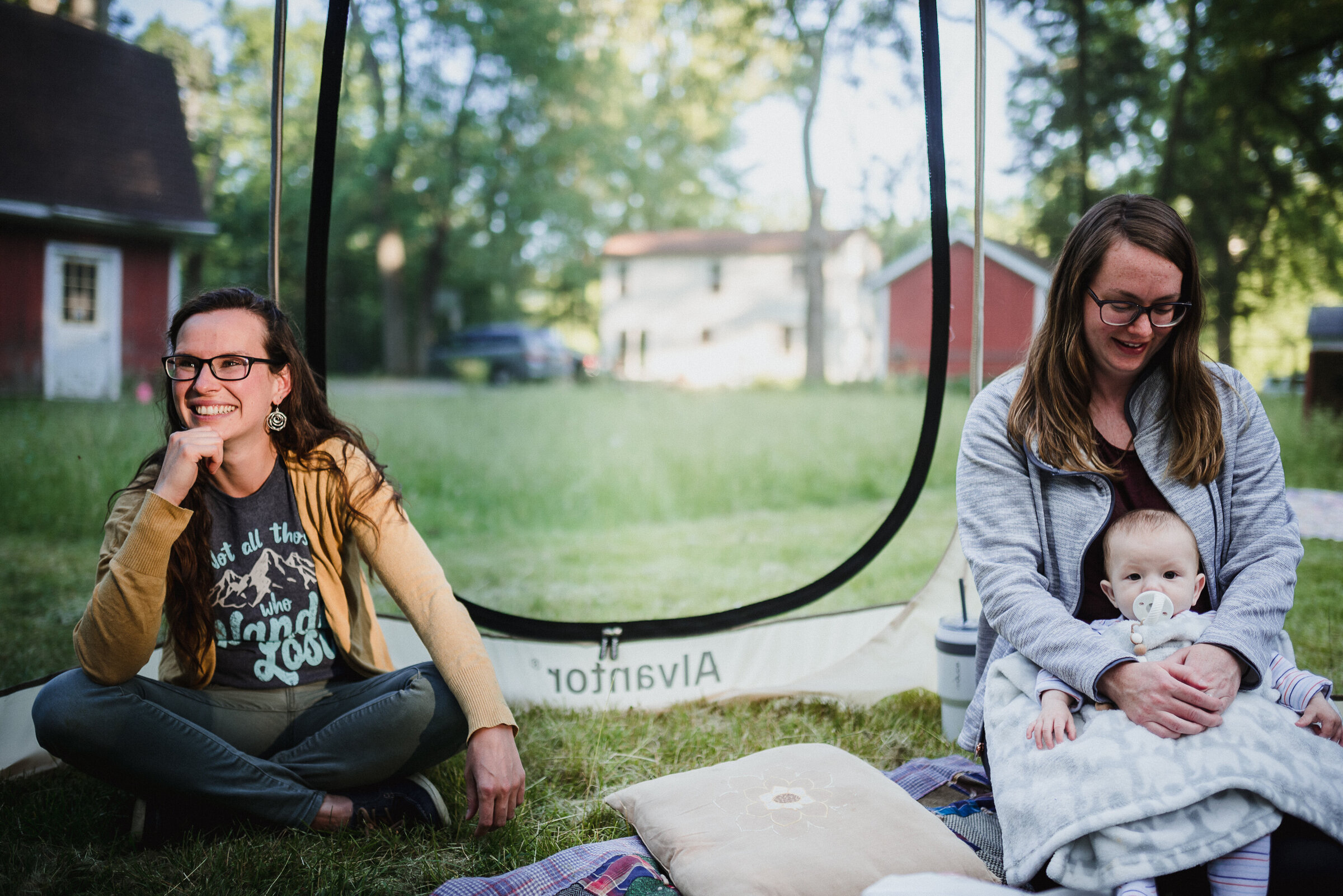 A young mother, her baby, and a mentor relaxing together at camp